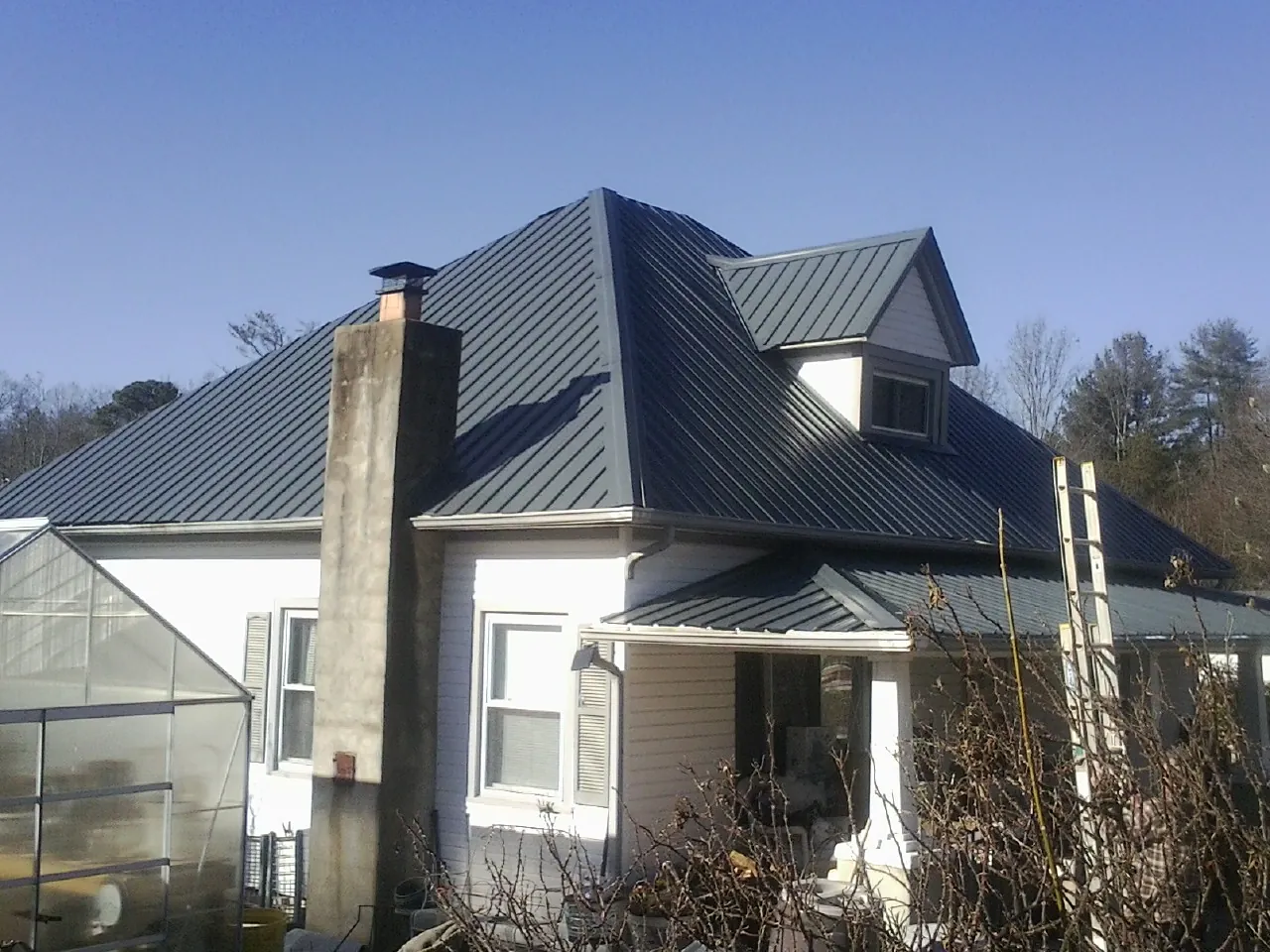 Dark blue standing seam metal roof on a white farmhouse with dormer — Slate & Tile Roof Repair by Roofing Brothers in Olyphant