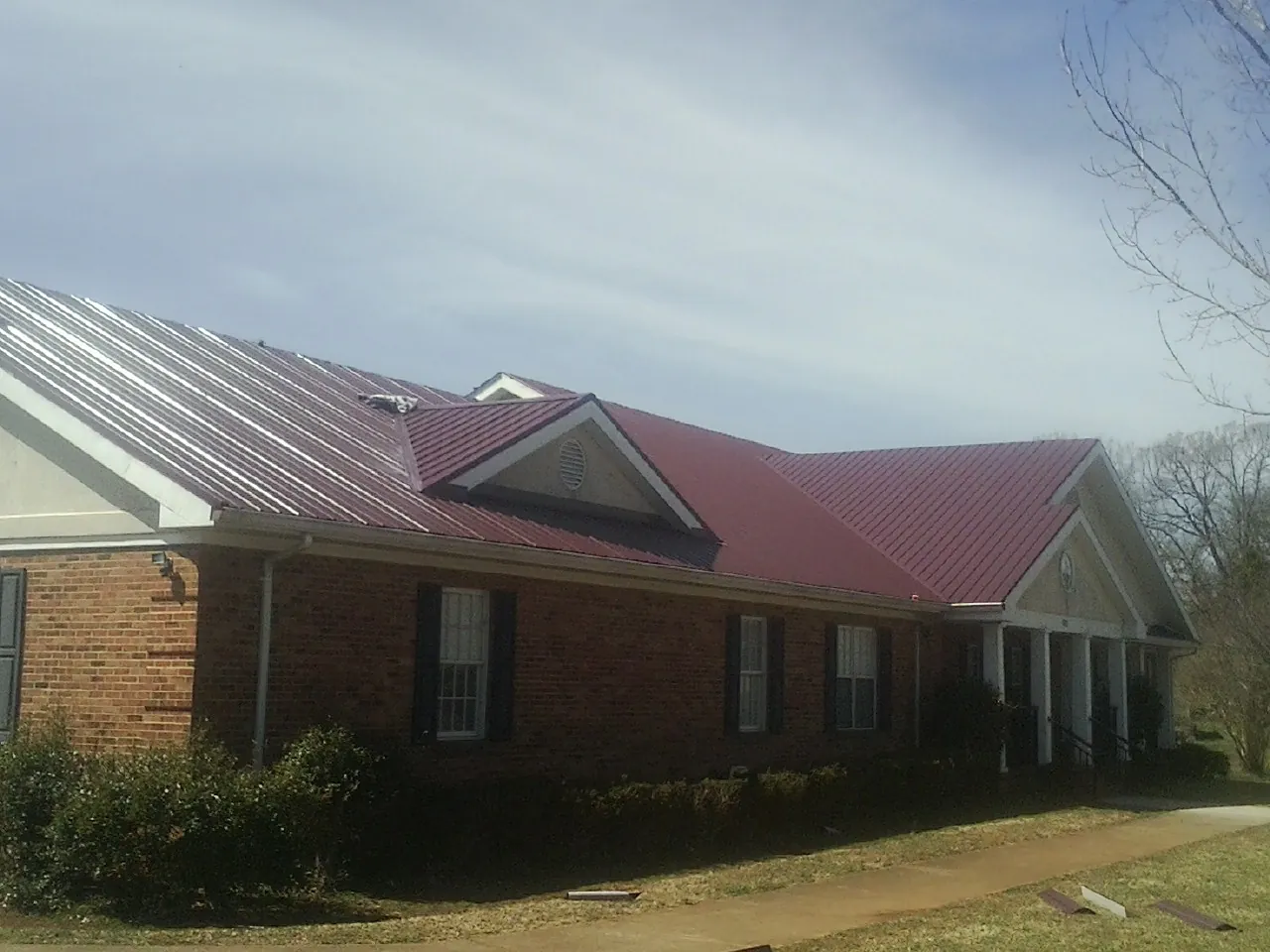 Red metal roof with gabled entries on a long brick building, from a Hail Damage Roof Repair job in Olyphant