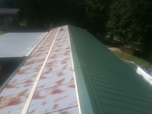 Old rusted panels beside newly installed green metal roofing — Wind Damage Roof Repair by Roofing Brothers in Olyphant