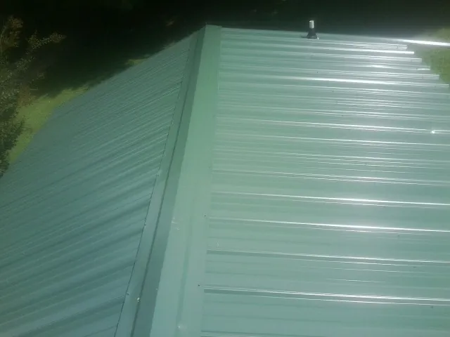 New green metal panels meeting at the ridge of a roof — Flat Roof Repair work by our crew in Olyphant