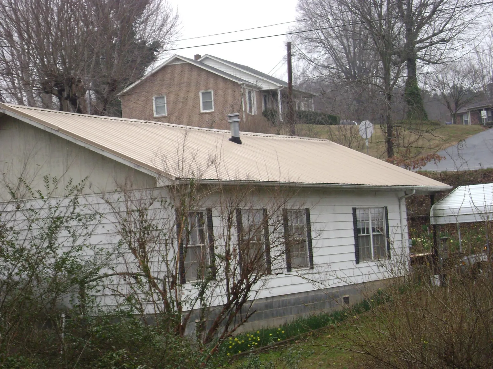 Tan metal roof on a white sided house set into a hillside — Commercial Roofing by Roofing Brothers in Olyphant